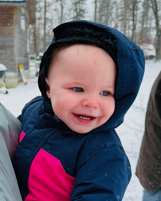 A smiling baby bundled up in the first snow